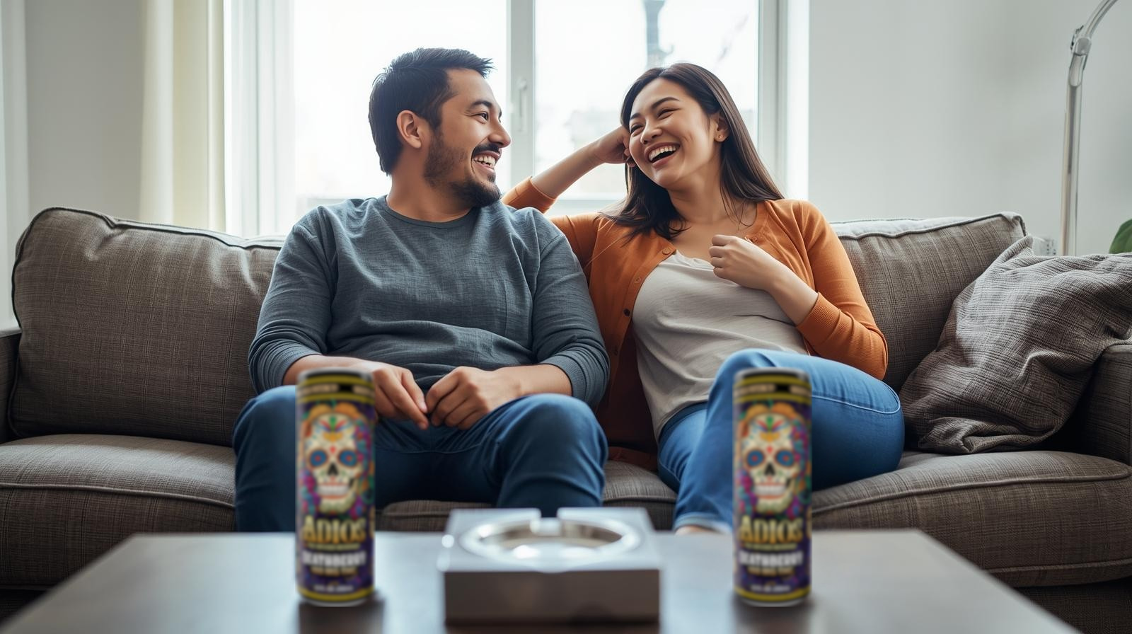 Man and woman sitting on a couch with two cans of ADIOS Deathberry in front of them.